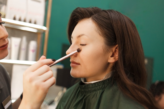 Make-up artist applies powder on the client’s skin with a makeup brush. Makeup process in a beauty salon