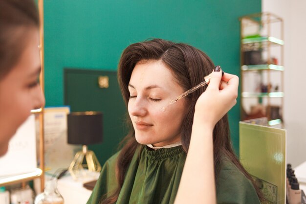 Make-up artist applying cosmetic oil on face of young woman. Applying makeup liquid foundation