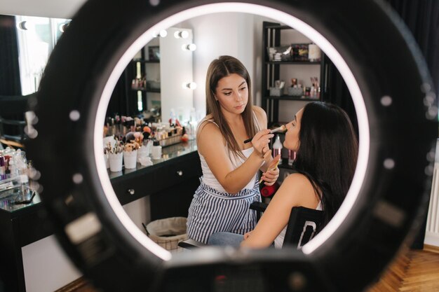 Photo make up artist making a makeup for attractive young girl beautiful young brunette woman ring lamp