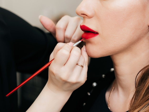 Make up artist puts red lipstick with brush on the lips of a woman