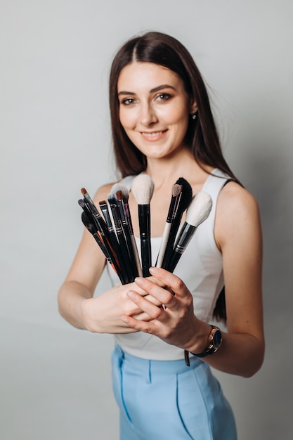 Make-up artist's brushes in the hands in the foreground. on a light wall