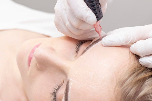 Make-Up. Beautician Hands Doing Eyebrow Tattoo On Woman Face.Permanent Brow Makeup In Beauty Salon. Closeup Of Specialist Doing Eyebrow Tattooing For Female. Cosmetology Treatment.