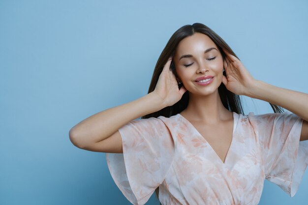 Make-up, beauty en mode concept. Het portret van ontspannen mooie vrouw houdt haar, staat met gesloten ogen, herinnert zich iets aangenaams, draagt modieuze kleding.