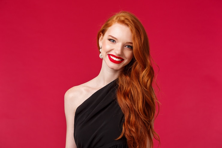 Foto make-up, beauty en vrouwen concept. close-up van elegante mooie roodharige vrouw in luxe slanke zwarte jurk, rode lippenstift, vrolijk en blij glimlachen, bijwonen van formele gebeurtenis, feest of romantische date
