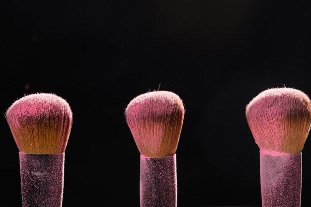 Make up, beauty and mineral cosmetic concept  brushes with pink powder over the black wall