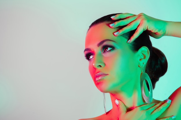 Make up and Beauty Woman with red and green neon light on her face with gold sparkle makeup and geometry earrings