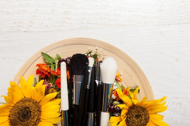 Make up brushes on plate next to wild flowers on wooden background