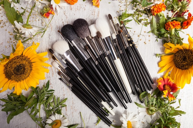 Make up brushes on wooden background next to wild flowers. Professional cosmetics