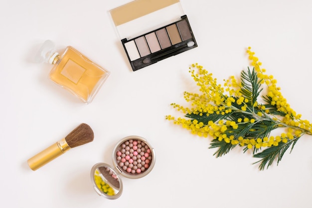 Make-up cosmetica hydrogel patches toilet water make-up kwasten en een tak van gele mimosa op een lichte achtergrond Flat lay fashion blogger