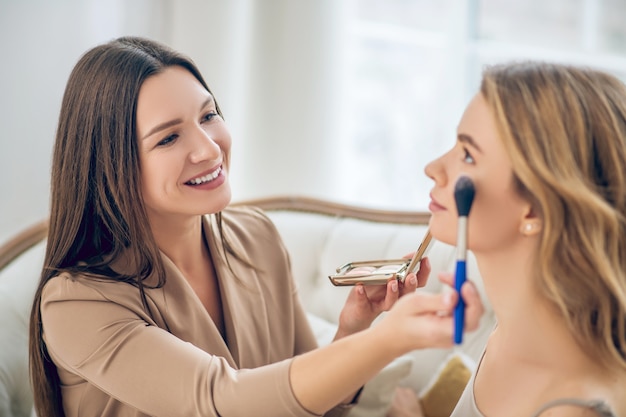 Make up. Dark-haired smiling girl doing make up to her friend