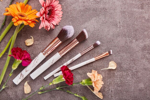 Make up kit brushes among flowers with copy space