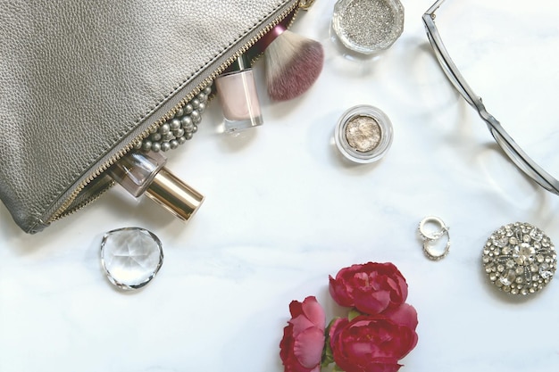 make-up kit with jewelry and eyeglasses by rose on white table