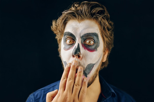 Make-up man van de dag van de dood op halloween, verbaasd kijken. geschokte blik en een hand voor zijn mond. kopieer ruimte