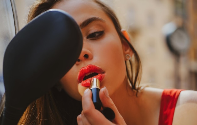 Make-up op wandeling stadsleven mode sexy meisje met rode lippen zet lippenstift in een spiegel van motorcy