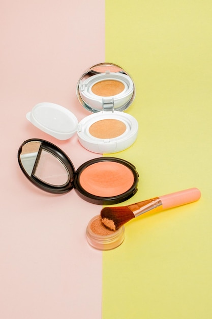 Make up products spilling on to a bright yellow and pink background with copy space