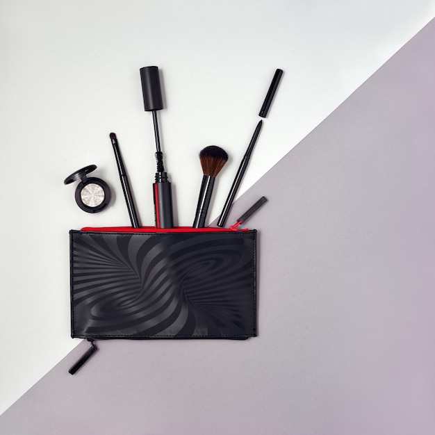 Make up products spilling out of a black cosmetics bag with empty space at right side Flat lay composition