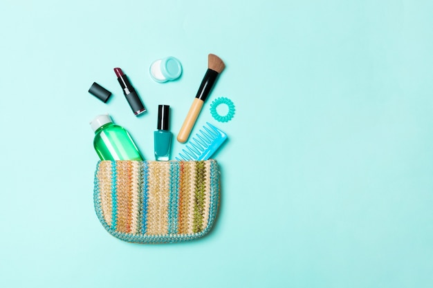 Make up products spilling out of cosmetics bag on blue pastel with empty space for your design