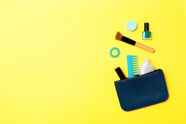 Make up products spilling out of cosmetics bag on yellow surface with empty space for your design