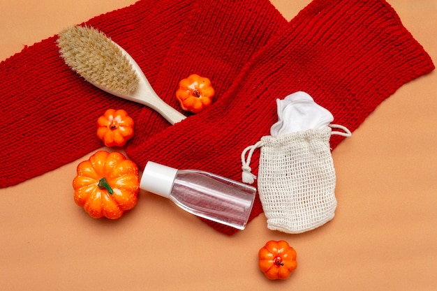 Make-up remover, borstel en natuurlijke herbruikbare sponzen in een zak op een beige achtergrond met een rode sjaal en oranje pompoenen. Herfst lay-out. Bovenaanzicht, vlak