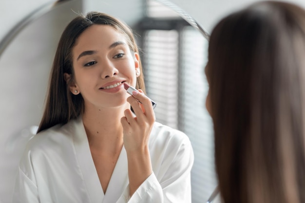 Make-up routine mooie jonge vrouw naakt lippenstift toe te passen op lippen in de buurt van spiegel