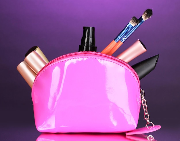 Make-up tas met cosmetica en borstels op violette achtergrond