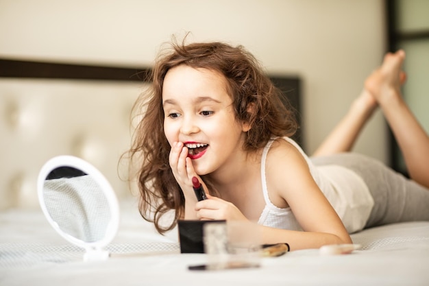 Foto make-up voor kinderen gelukkige schattige meisje die make-up doet ligt op het bed in de slaapkamer