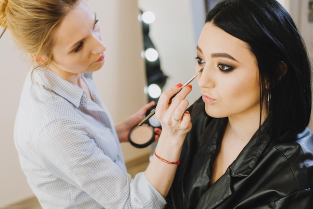 Make-upmeester die make-up doet aan mooi model indoor schoonheidsstudio