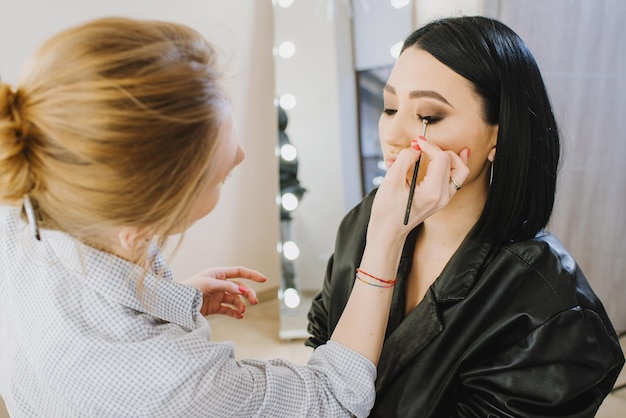 Make-upmeester die make-up doet aan mooi model indoor schoonheidsstudio