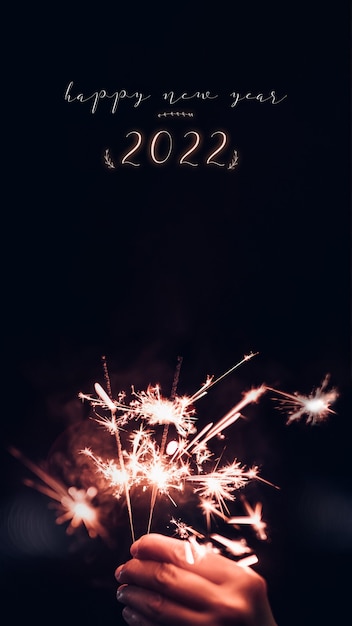 Foto esprimi un desiderio per il nuovo anno 2022 con la mano che tiene in mano un'esplosione di fuochi d'artificio sparkler con su uno sfondo nero bokeh di notte, festa evento festa. rapporto verticale