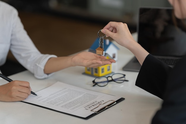 Makelaar die huissleutel aan zijn cliënt houdt na ondertekening van de contractovereenkomst in officeconcept voor onroerend goed dat naar huis verhuist of onroerend goed huurt