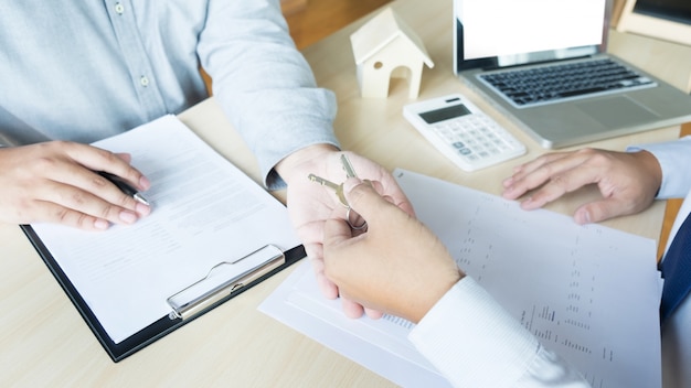 Makelaar in kostuumsitting in een bureau. overhandiging van huis sleutels met klant na contract handtekening