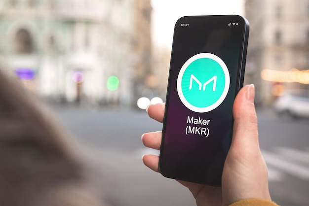 Maker MKR cryptocurrency symbol, logo. Business and financial concept. Hand with smartphone, screen with crypto icon close-up