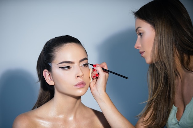 Makeup artist applies eye shadow hand of visagiste painting cosmetics of young beauty model girl fas