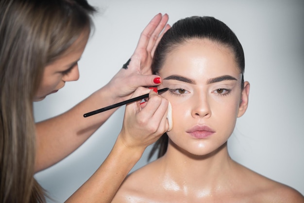 Makeup artist applies eye shadow hand of visagiste painting cosmetics of young beauty model girl nat