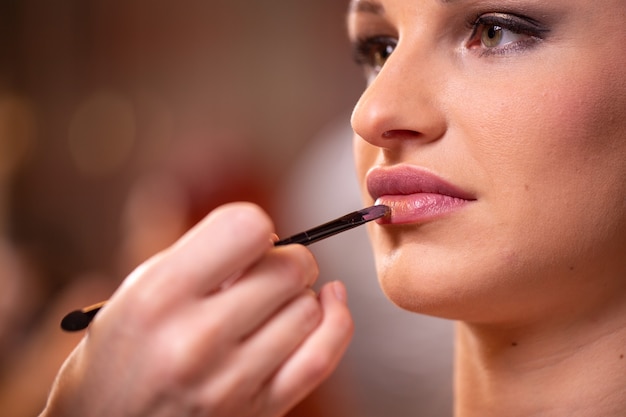 Makeup artist applies pink gloss lipstick