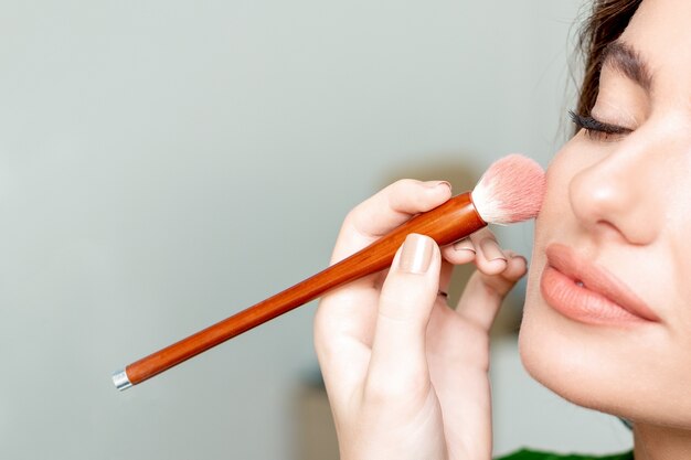 Makeup artist applies skin tone makeup on woman's face with copy space close up