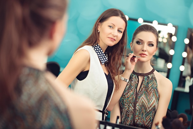 Makeup artist applying lipstick with a brush on model's lips