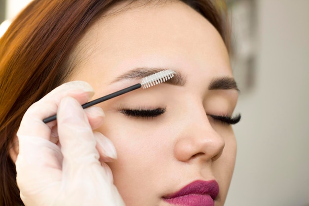 The makeup artist combs his eyebrows with a brush. Eyebrow styling. Permanent makeup. Coloring with henna paint.