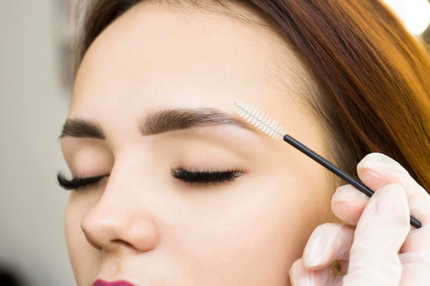 The makeup artist combs his eyebrows with a brush. Eyebrow styling. Permanent makeup. Coloring with henna paint.