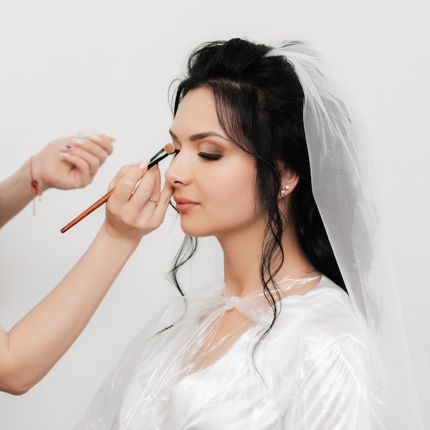 Le mani del truccatore con un pennello compongono e applicano le ombre sugli occhi della ragazza delle spose nel salone di bellezza