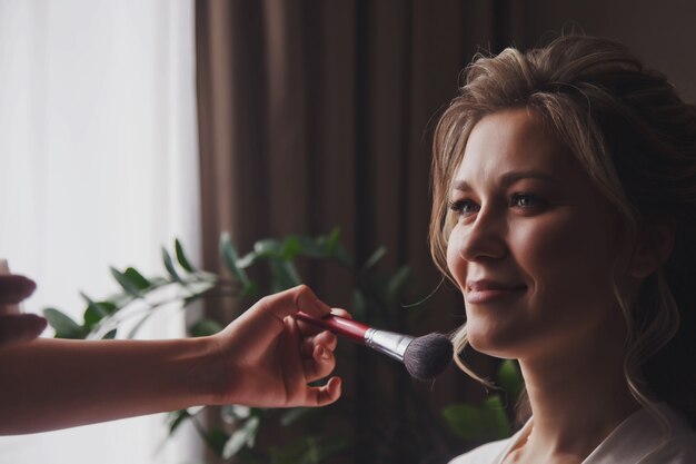 Makeup artist made wedding make-up for cute young woman bride at wedding day in hotel room