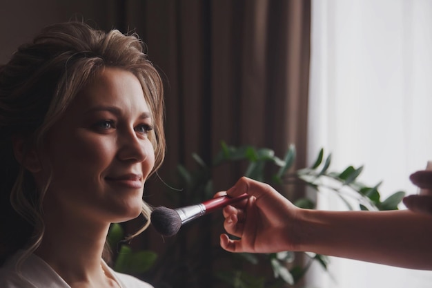 Makeup artist made wedding makeup for cute young woman bride at wedding day in hotel room