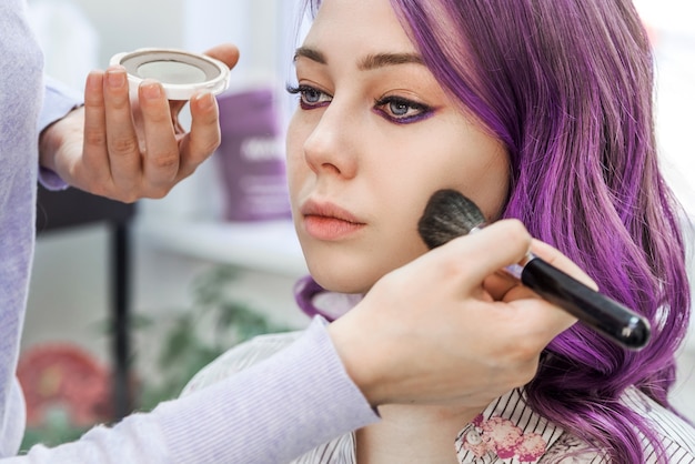 makeup artist makes up an attractive woman with colored lilac hair