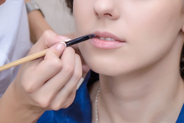 Makeup artist paints girl's lips with a brush