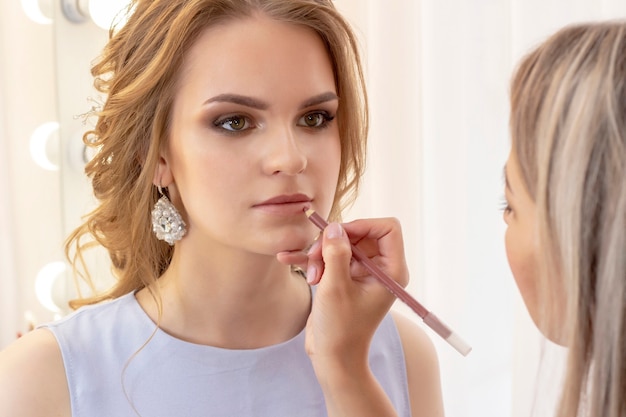 Foto il truccatore dipinge il modello delle labbra con la fodera per le labbra. trucco in delicate tonalità beige neutre da giorno