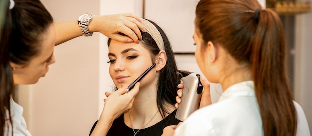 Makeup artist using an airbrush on the face of a young caucasian woman in a beauty salon