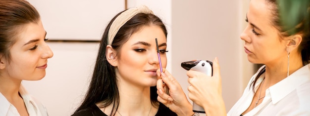 Foto truccatore usando un aerografo sul viso di una giovane donna caucasica in un salone di bellezza