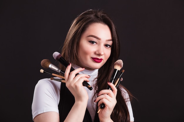 Makeup artist with brushes in hand on a black wall