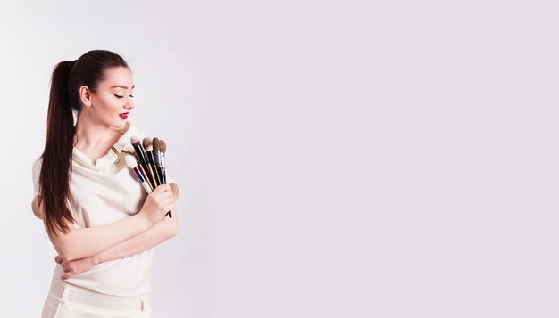 Makeup artist with brushes in hand on a white wall