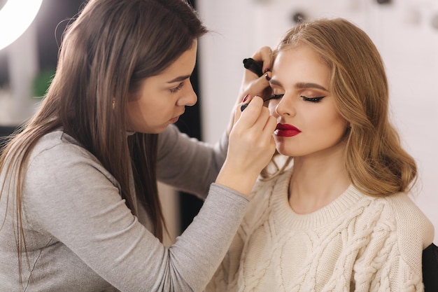 Trucco artista lavoro in studio di bellezza donna che si applica da un maestro di trucco professionale bella truccatrice fare un trucco per il modello di capelli biondi